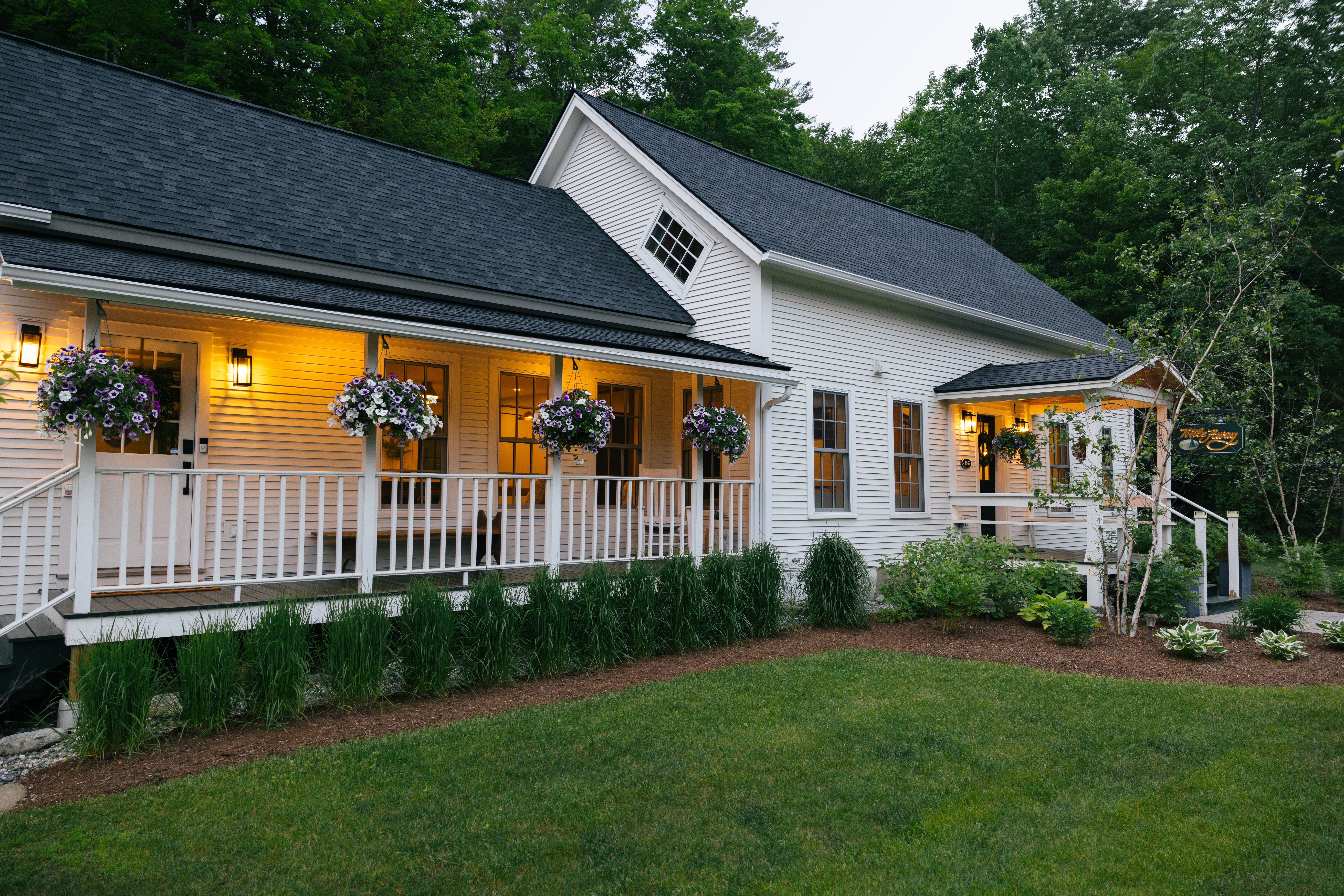 Front exterior of the Mile Away farmhouse with wraparound porch and hanging flower baskets